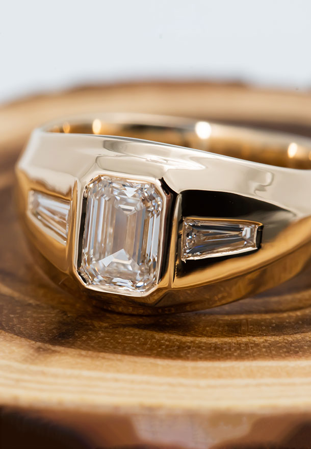 a yellow gold ring with a bezel set emerald cut diamond on a block of wood