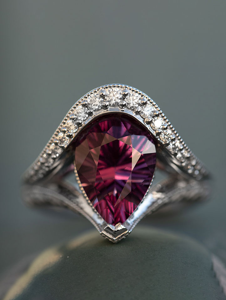 a close up of a white gold ring with a pear-shaped pink tourmaline